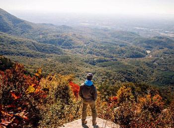 A hiker overlooking a valley of colorful trees in autum.