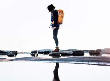 A hiker looking into a body of water, thier reflection showing under them.