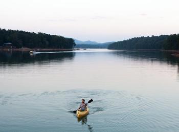 A kayaker in a still, open lake lined with trees