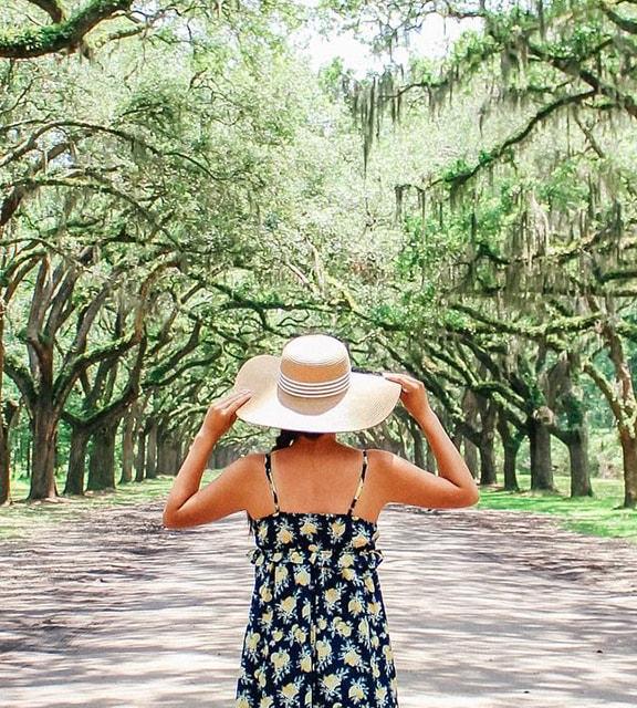 Girl with large straw sun hat look up a tree lined road