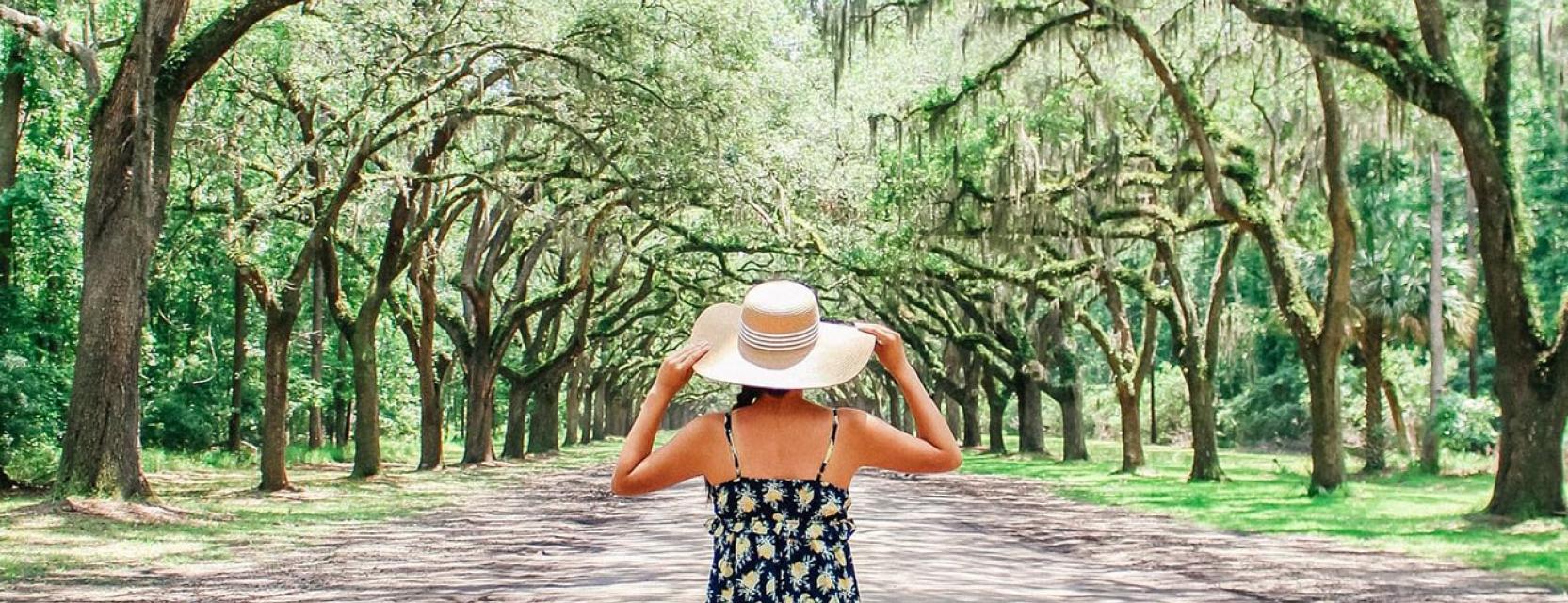 Girl with large straw sun hat look up a tree lined road
